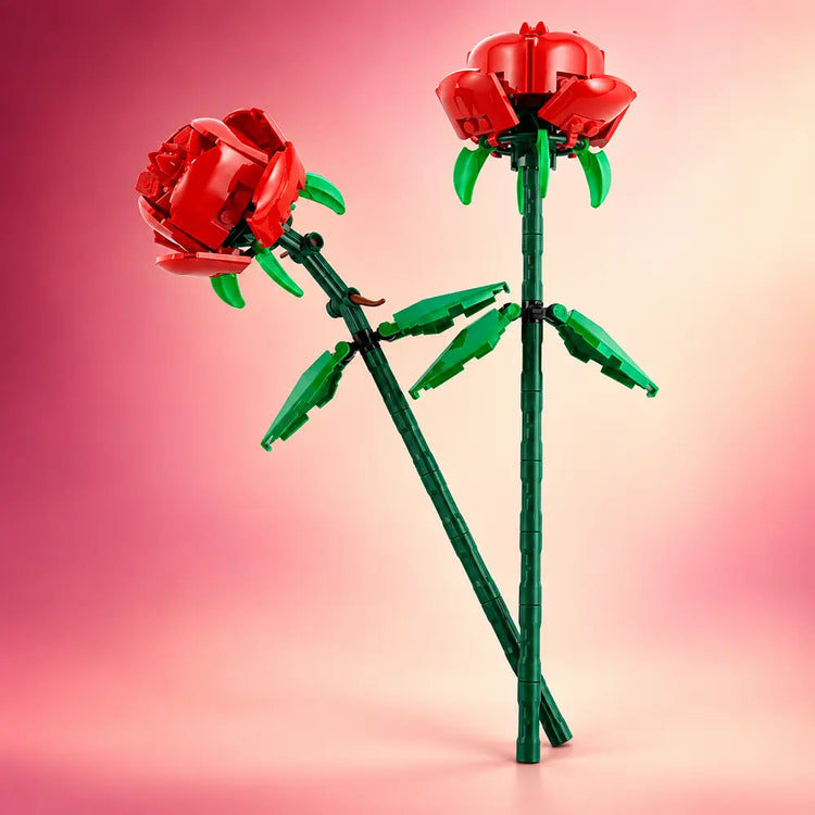 Twee rode LEGO® rozen met groene stelen uit set 40460 tegen een roze achtergrond